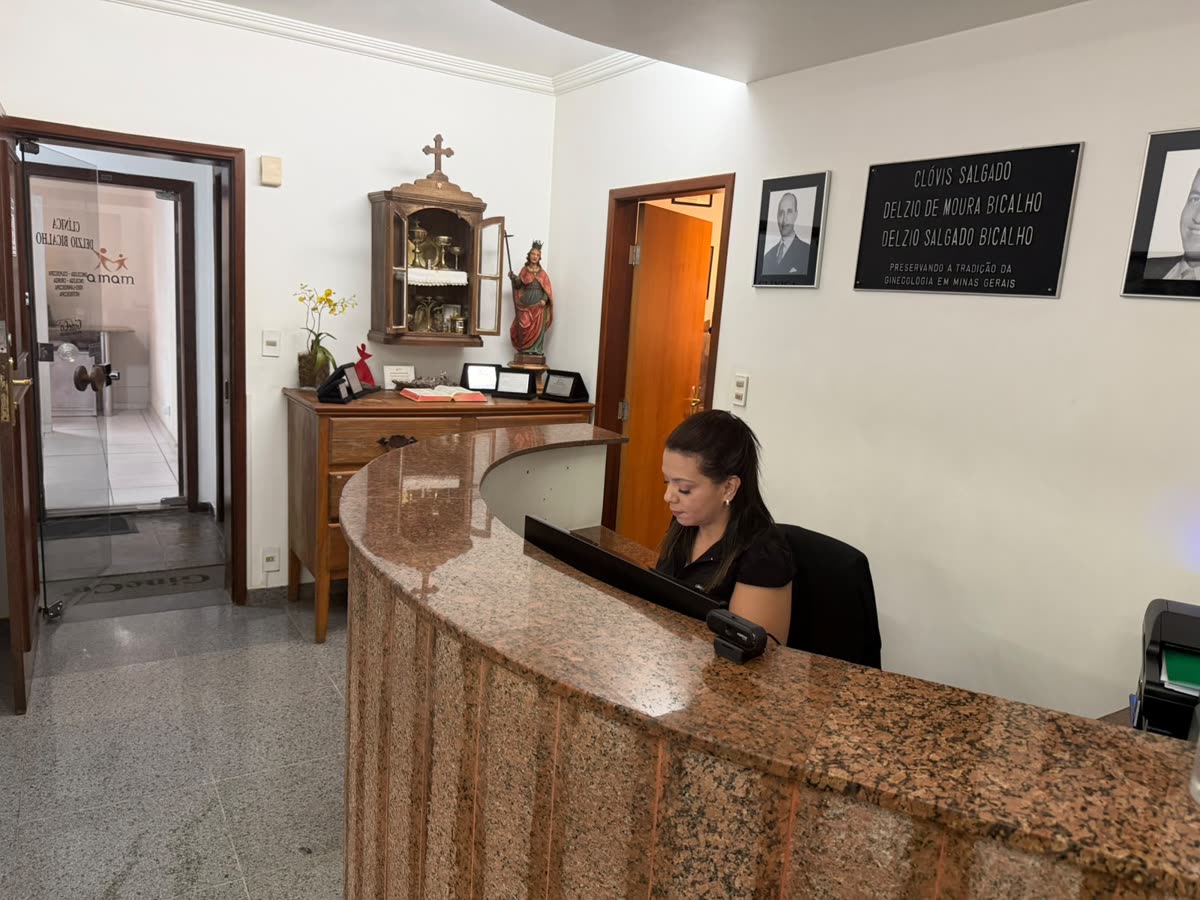 Hall de entrada da clínica com o balcão de granito, o oratório, a placa da linhagem e os retratos na parede