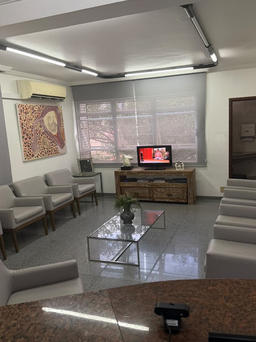 Sala de estar da clínica com poltronas claras dispostas ao longo das paredes, televisão e janela ampla